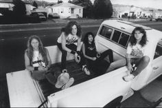 four young women sitting on the back of a car in front of a white van