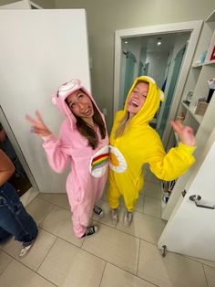 two girls dressed in costumes standing next to each other on the bathroom floor with their hands up