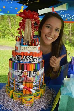 a woman is posing next to a large cake made out of crayons and markers