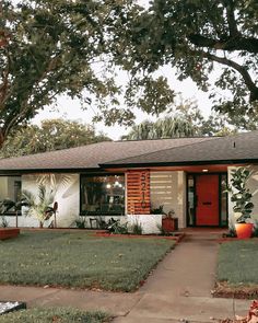 a red door sits in the front yard of a white house with green grass and trees