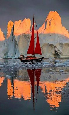 a sailboat with red sails in front of icebergs