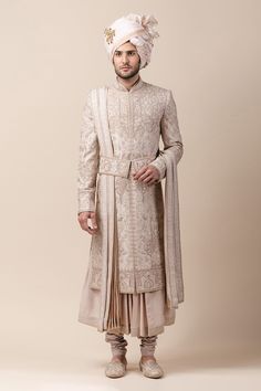 a man wearing a turban and standing in front of a beige background