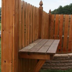 a wooden bench sitting on top of a lush green field next to a tall fence