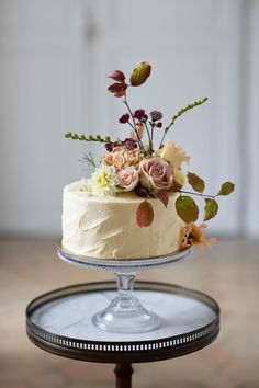 there is a cake with flowers on it sitting on a glass platter that has a metal stand