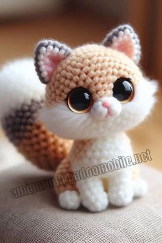 a small crocheted cat sitting on top of a cushion with eyes wide open