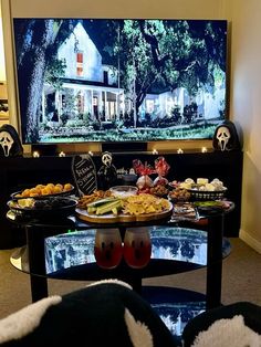 a table with food on it in front of a large screen tv that is turned on