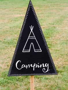 a black and white sign that says camping with a teepee tent in the background