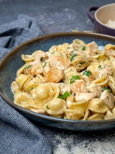 pasta with chicken and spinach in a blue bowl next to a cup of coffee