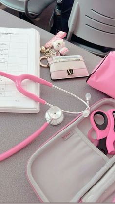 pink scissors and other items are sitting on a table in front of a notebook with a stethoscope next to it