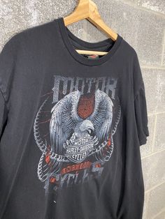 a black t - shirt with an eagle on it hanging from a wooden hanger