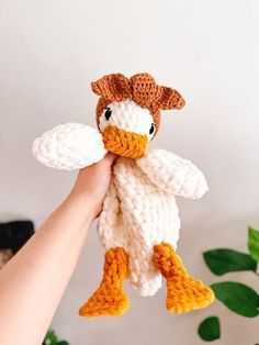 a hand holding a crocheted stuffed duck in it's beak and wings