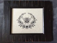 a black frame with a drawing of a bee on it's side and flowers in the middle