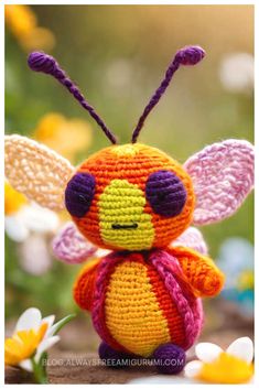 a small crocheted bee sitting on top of a wooden table next to flowers