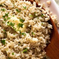 a wooden spoon filled with rice on top of a white plate and topped with parsley