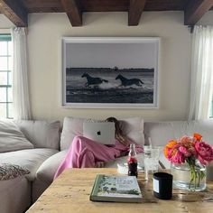 a woman sitting on a couch in front of a table with flowers and an open laptop