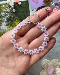 a hand holding a bracelet with pink flowers on it