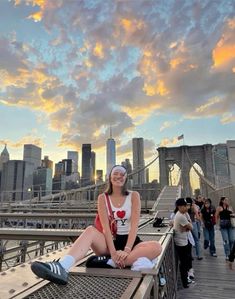 a woman sitting on the edge of a bridge in front of a cityscape