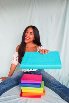 a woman sitting on the floor holding up a blue bag with five different colored bags in front of her