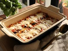 a casserole dish with meat and cheese in it sitting on a table next to a potted plant