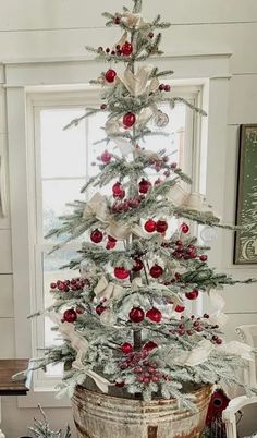 a white christmas tree with red ornaments in a bucket