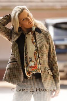 Woman wearing a plaid jacket and colorful scarf with a pheasant design, standing outdoors.