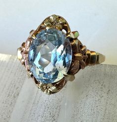 a most lovely ring with an equally lovely aquamarine in a three gold creation, likely made in the 1920's.  the shank and frame of this beauty is yellow gold, testing @ 10k.  the little bows to the sides of the stone are rose gold, and the forget-me-not flowers at top and bottom are green gold.  the stone is a beautifully clear aquamarine in almost perfect condition.  i can see two very tiny flea bites on facet edges, and that's with magnification.  the stone is set with four prongs in a beautifu Aquamarine Gem, Bow Ring, Evil Eye Pendant, Almost Perfect, Lovely Ring, Forget Me Not, Perfect Ring, Ring Size 7, Green Gold