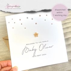 a hand holding up a baby shower card with gold stars on it and the words welcome to the world written in cursive writing