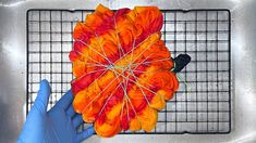 a person in blue gloves is holding an orange and red flower on a wire rack