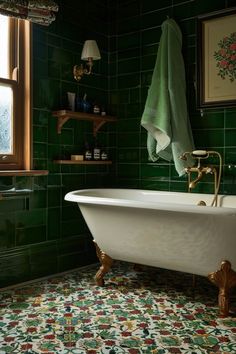 a bath tub sitting next to a window in a green tiled bathroom with gold fixtures