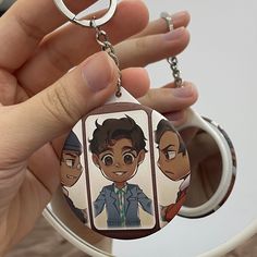 a person holding a keychain with three avatars on it