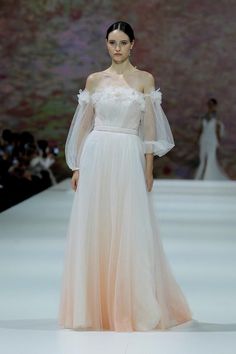 a woman in a white dress walking down a runway