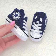 a hand is holding up a tiny crocheted blue and white shoe with the word converse written on it