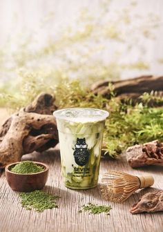 a cup filled with green tea sitting on top of a wooden table next to other items