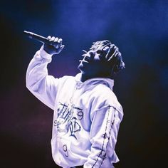 a man in a white hoodie holding a microphone up to his ear while standing on stage