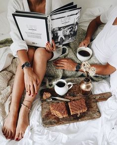 two people sitting on a bed with coffee and books in their hands, one reading a book