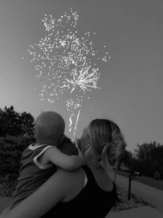 a woman holding a child in her arms watching fireworks