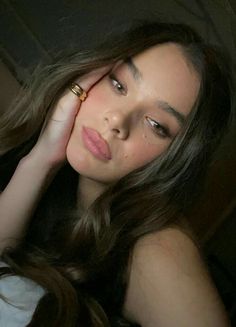 a beautiful young woman laying on top of a bed next to a white pillow with her hand near her face