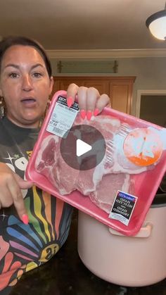 a woman holding up a pink tray with meat in it