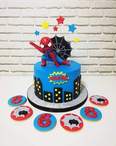 a spiderman themed birthday cake and cupcakes on a table with white brick wall in the background