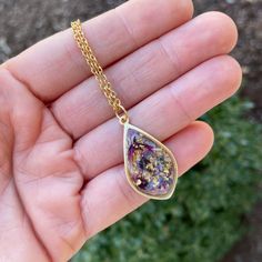 a hand holding a gold filled necklace with flowers on it and a chain attached to it