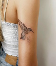 a woman's arm with a small hummingbird tattoo on the back of her left arm