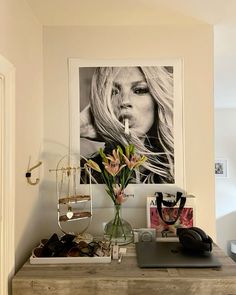 a desk with a vase and flowers on it in front of a framed photo above the desk