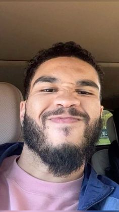 a man with a beard sitting in the back seat of a car looking at the camera