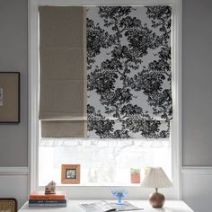 a white desk topped with a lamp next to a window covered in black and white curtains