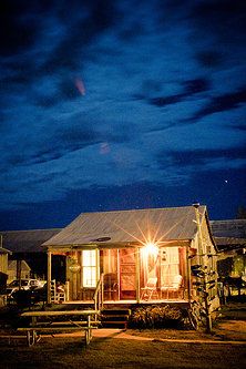 a small cabin is lit up at night with the moon in the sky behind it