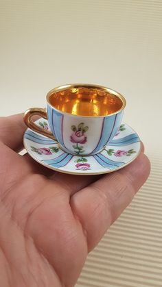 a hand holding a miniature tea cup and saucer