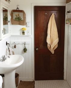 a white sink sitting under a bathroom mirror next to a wooden door with towels hanging on it