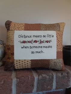 a pillow with a message on it sitting on top of a brick wall next to a vase