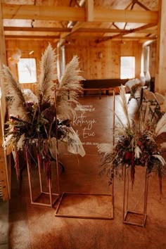 two tall vases filled with flowers and feathers on top of a wooden floor next to a chalkboard