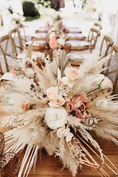 an arrangement of flowers and feathers is on the dining table at this outdoor wedding reception